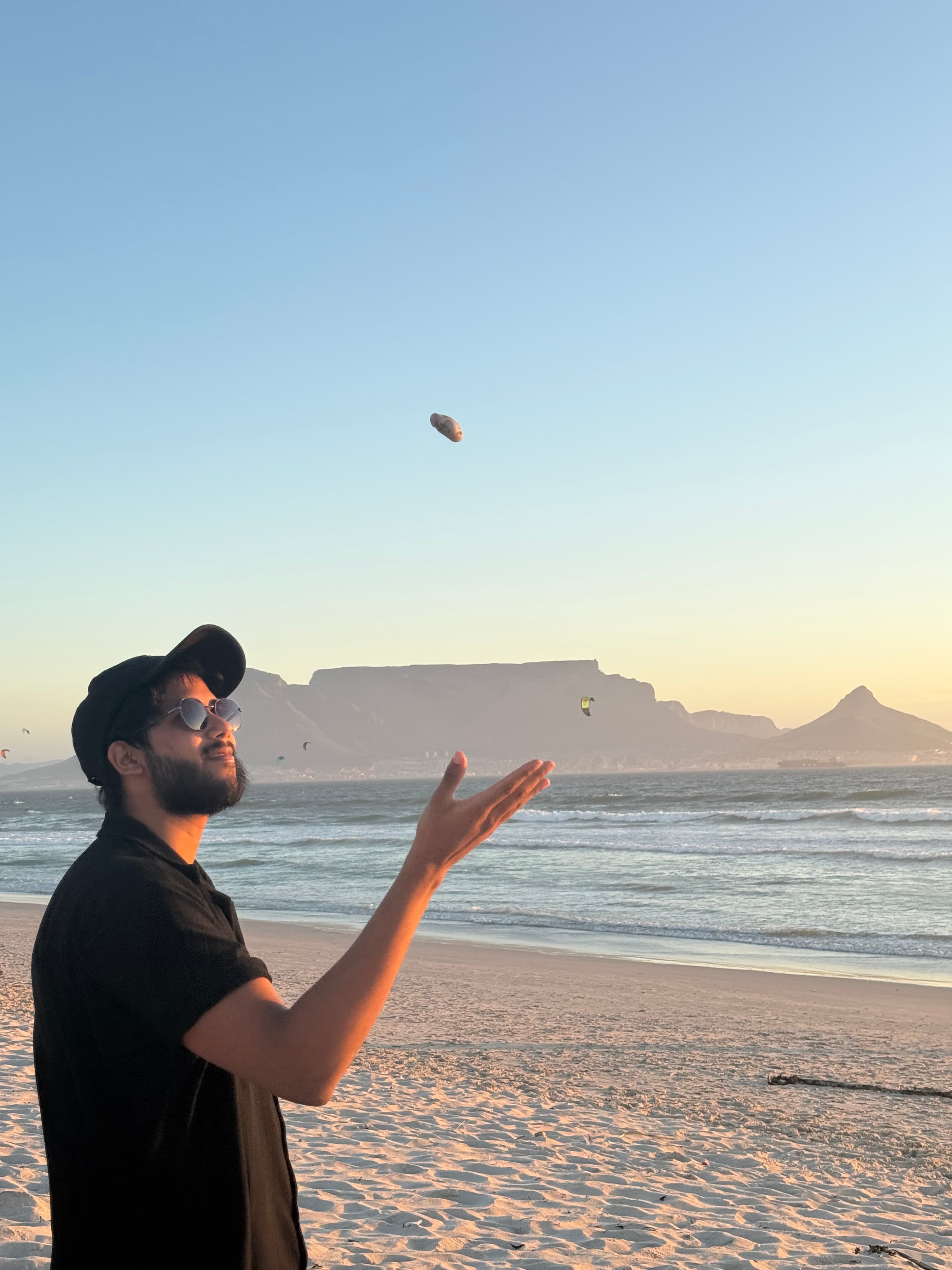 Akhil tossing a stone on Blouberg beach with Table Mountain behind him